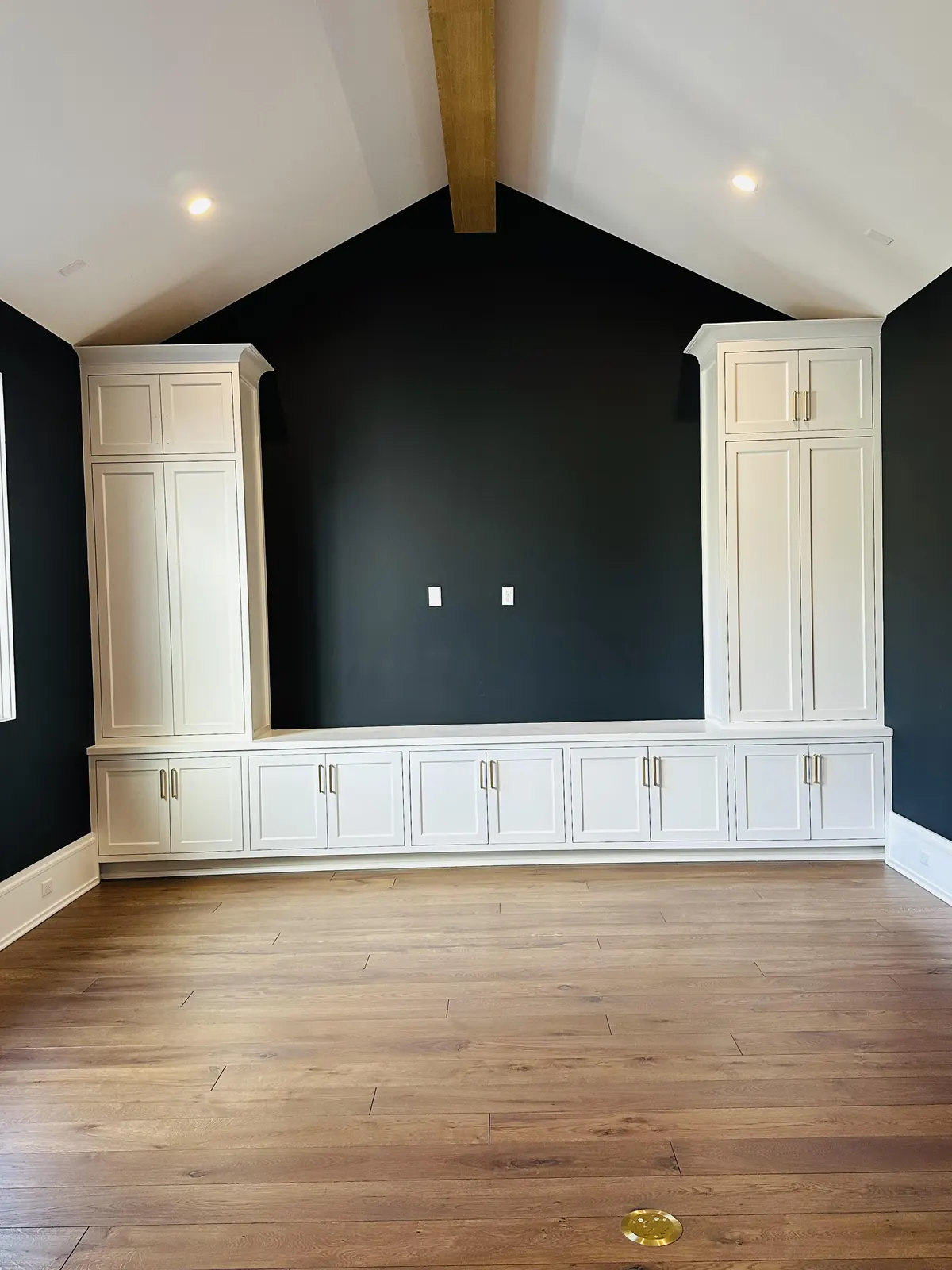Dark accent wall between white built-in cabinets under a beamed ceiling