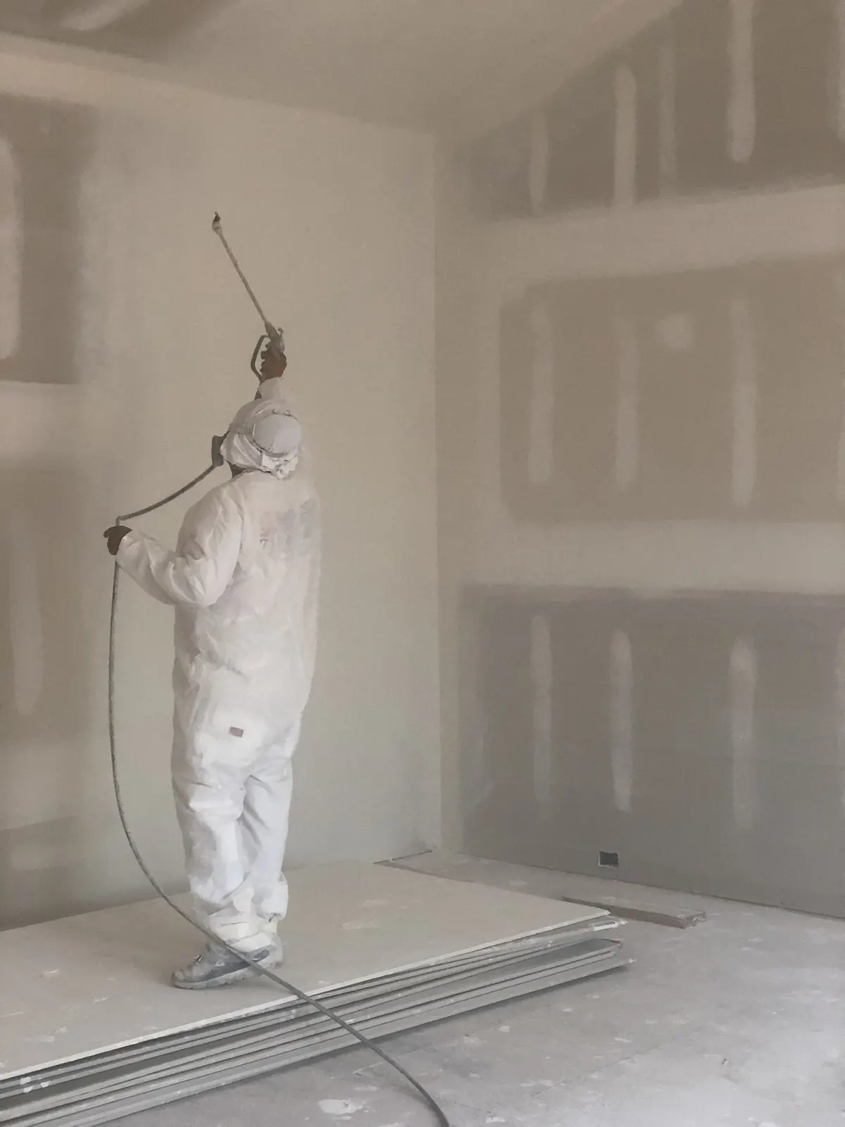 Painter in protective gear spraying primer on new drywall
