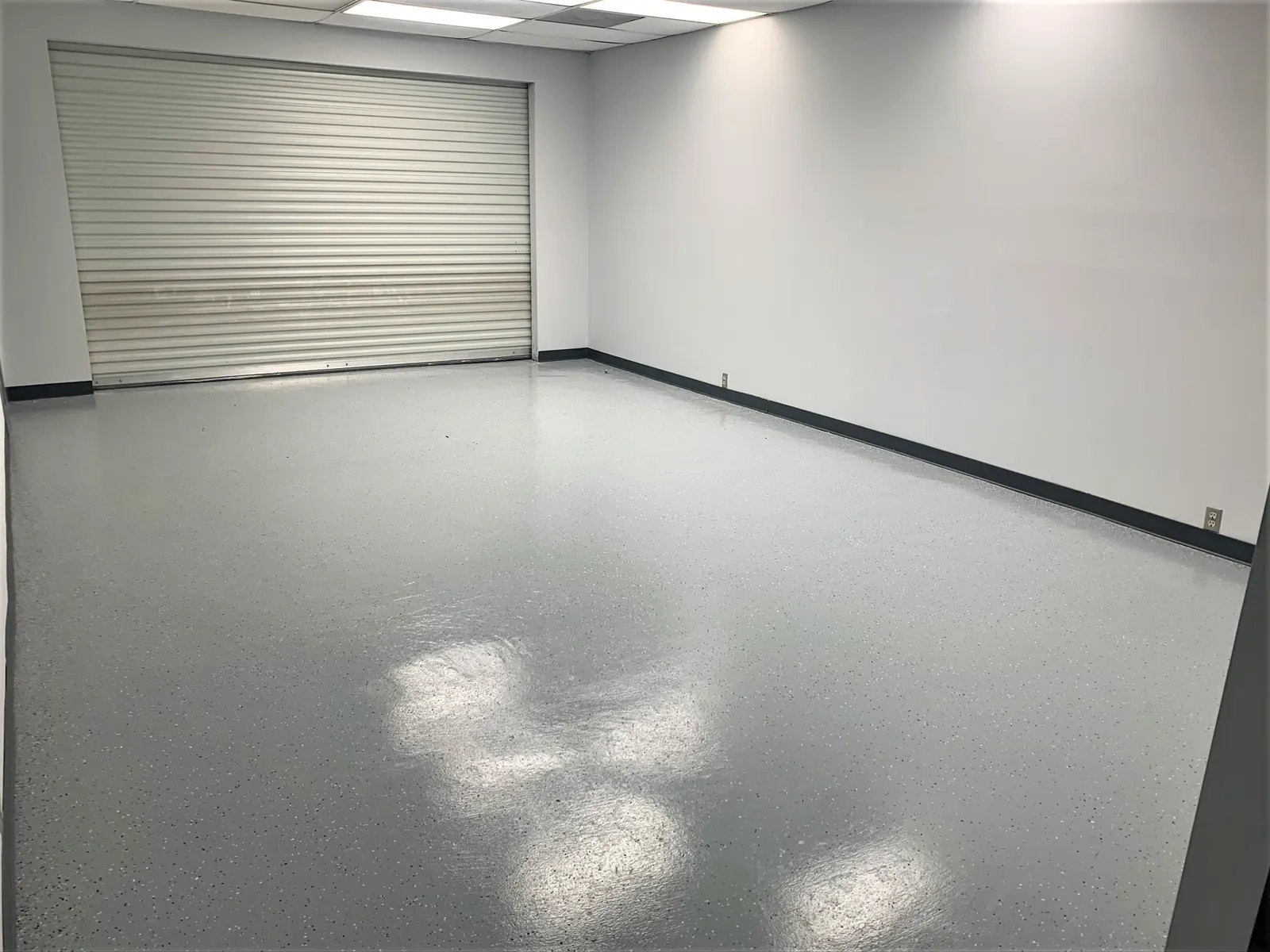 Gray epoxy floor in a large garage room with a roll-up door
