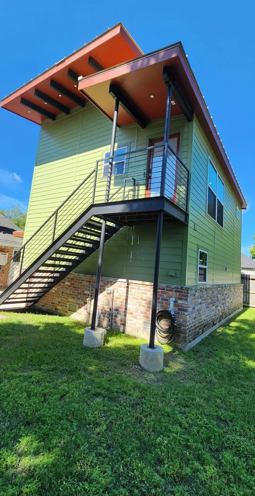 Modern two-story home painted green with a red soffit and exterior stairs